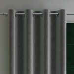 Zasłona welwetowa w ciemno szarym kolorze o wymiarach 140x260 cm, zawieszona na przelotkach. Ujęcie frontalne, ukazujące strukturalną teksturę tkaniny. W tle widoczny zielony element, co podkreśla kontrast zasłony w aranżacji wnętrza.