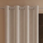 Zasłona welwetowa kremowa 140x260 cm na przelotkach, wisząca, z miękkiego materiału. Kąt ujęcia frontalny. Widoczne przelotki do zawieszenia na karniszu. Tło w odcieniu beżowym, podkreślające kolor zasłony. Brak widocznych napisów lub zdobień.