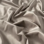 Szaro-beżowa welwetowa zasłona w miękkiej tkaninie Velvi, rozłożona, z wyraźną teksturą, bez wzorów. W tło neutralne, podkreślające elegancję materiału oraz możliwe zastosowanie w aranżacji wnętrz. Rozmiar: 140x260 cm.