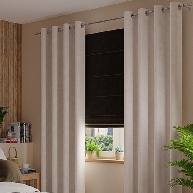 Zasłona gotowa welwetowa w jasnoszarym kolorze, o wymiarach 140x260 cm, zawieszona na przelotkach. Produkt widoczny w aranżacji z drewnianym tłem, obok okna z roletą, roślinami oraz książkami na półce. Tekstura welwetu jest miękka i matowa.