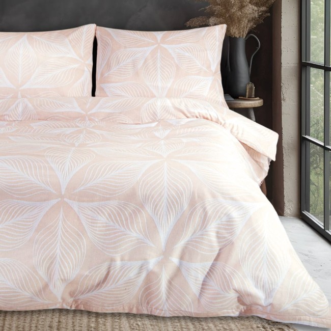 Pościel flanelowa 220x200 w pudrowym różu z białymi liśćmi, rozłożona na łóżku. Dwie poszewki na poduszki oraz kołdra z delikatnym wzorem roślinnym. Niezwykle miękka faktura materiału, widoczna na tle szarej ściany i okna z naturalnym światłem.