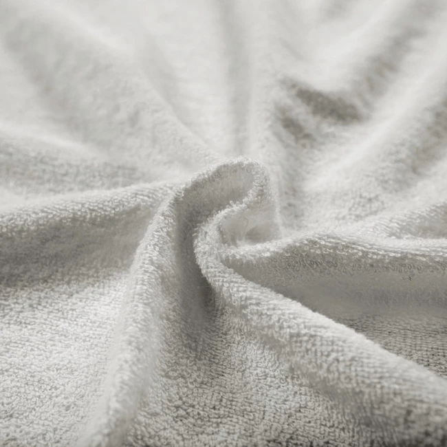 Szara pościel frotte 160x200, prezentująca gładką, teksturowaną powierzchnię. Ułożona w lekki sposób, podkreślająca miękkość materiału. Brak widocznych napisów i logo. Zdjęcie na prostym tle, co uwydatnia detal i fakturę tkaniny.