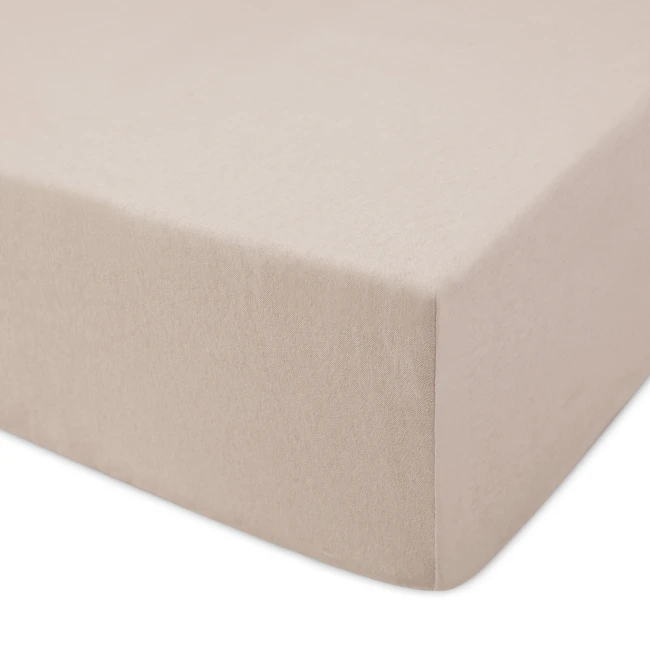 Prześcieradło jersey z gumką 120x200 w kolorze beżowym, rozłożone na materacu. Zbliżenie na teksturę materiału, pokazujące elastyczne boki oraz gładką powierzchnię. Prosty, jasny kontekst, podkreślający kolor i fakturę.