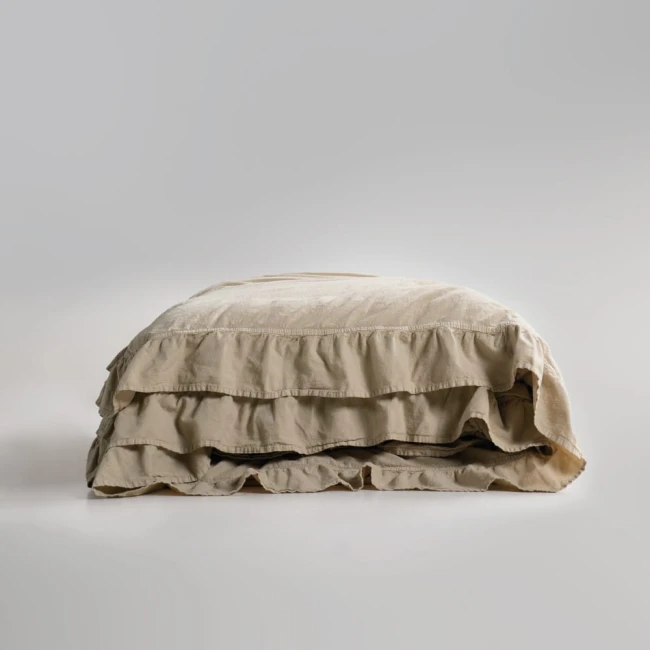Pościel bawełniana z falbanką w odcieniu beżowym, rozmiar 160x200 cm, złożona w formie prostokąta. Materiał teksturowany, wykończony dekoracyjną falbanką na brzegu. Produkt na jednolitym, jasno-szarym tle.