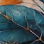 Poszewka satynowa 40x40 Satynlove Premium z wzorem przedstawiającym złote i turkusowe liście. Zdjęcie z bliska ukazuje detale faktury tkaniny oraz kontrastujące kolory. Gładka powierzchnia z widocznymi wąsami liści. Tło jest jasne i stonowane.