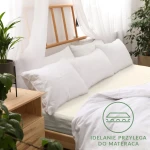 Prześcieradło jersey z gumką w kolorze ecru, o wymiarach 200x220 cm, rozłożone na łóżku. Ujęcie z boku ukazuje gładką fakturę materiału, dopasowującego się do materaca.