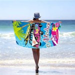 Ręcznik plażowy 100x180 Aloha Love z mikrofibry, przedstawiony z tyłu, rozłożony na plaży. Kolorowy wzór z fioletowym samochodem, napisami „Aloha” i „Surf Paradise”, palmami oraz falami. Osoba w kapeluszu stoi na brzegu morza, trzymając ręcznik.