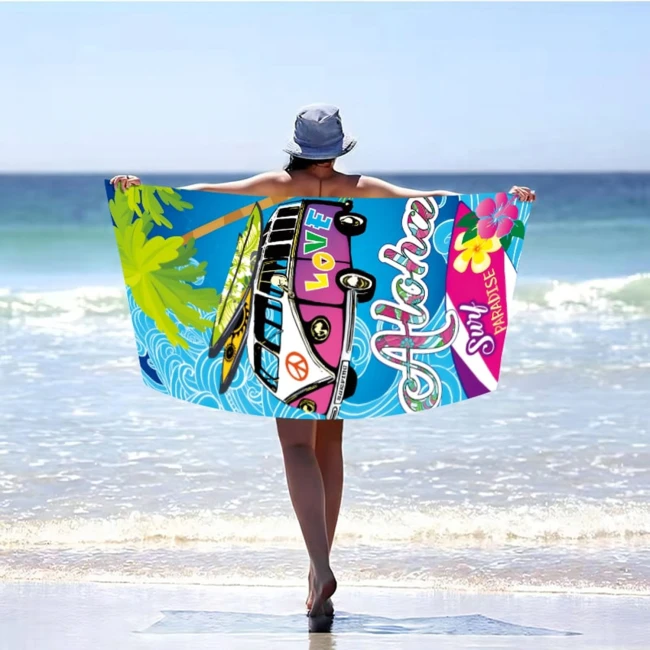 Ręcznik plażowy 100x180 Aloha Love z mikrofibry, przedstawiony z tyłu, rozłożony na plaży. Kolorowy wzór z fioletowym samochodem, napisami „Aloha” i „Surf Paradise”, palmami oraz falami. Osoba w kapeluszu stoi na brzegu morza, trzymając ręcznik.