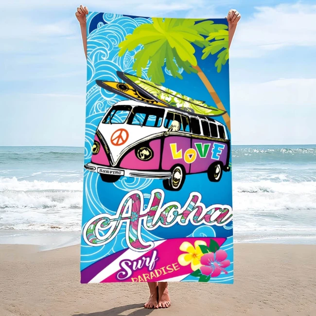 Ręcznik plażowy 100x180 cm, z mikrofibry, w kolorze niebieskim z grafiką surfingu, kwiatami i napisem Aloha Love. Złożony w pionie, trzymany przez osobę na plaży, z falami i palmami w tle. Szybkoschnący materiał idealny na plażę.