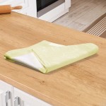 Ścierka bawełniana kuchenna w kolorze zielonym, z fakturą materiału, złożona w kształcie trójkąta na drewnianym blacie. Wzór przedstawia różne akcesoria kuchenne w jasnym kolorze. Produkt leży poziomo w aranżacji kuchennej. Wymiary 50x70 cm.