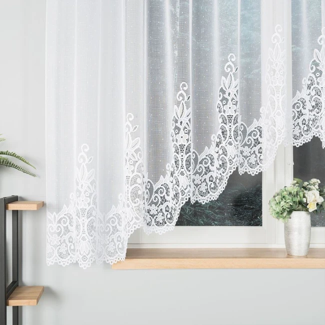 Firana gotowa BERENIKA żakardowa, o wymiarach 400x160 cm, w kolorze białym. Zawieszona na oknie, z haftowanym wzorem na dolnej krawędzi. Tło neutralne, z wazonem oraz rośliną w pobliżu. Przez firanę prześwituje światło, nadając przytulności wnętrzu.