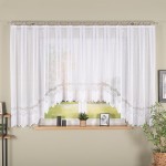 Firana gotowa MODESTA żakardowa, 400x160 cm, w kolorze białym, zawieszona na karniszu. Zdobiona dekoracyjnym wzorem na dolnej krawędzi. Widok frontalny, z tłem okna, które wpuszcza naturalne światło do wnętrza. Na parapecie widoczne doniczki i zdjęcia.