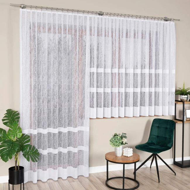 Firana gotowa WIKTORIA, żakardowa, biała, o wymiarach 200x250 cm, zawieszona na karniszu. Wzór z cienkimi liniami na delikatnej tkaninie. Ujęcie frontalne, firana rozłożona, w aranżacji wnętrza z zielonymi roślinami, stolikiem oraz krzesłem w tle.