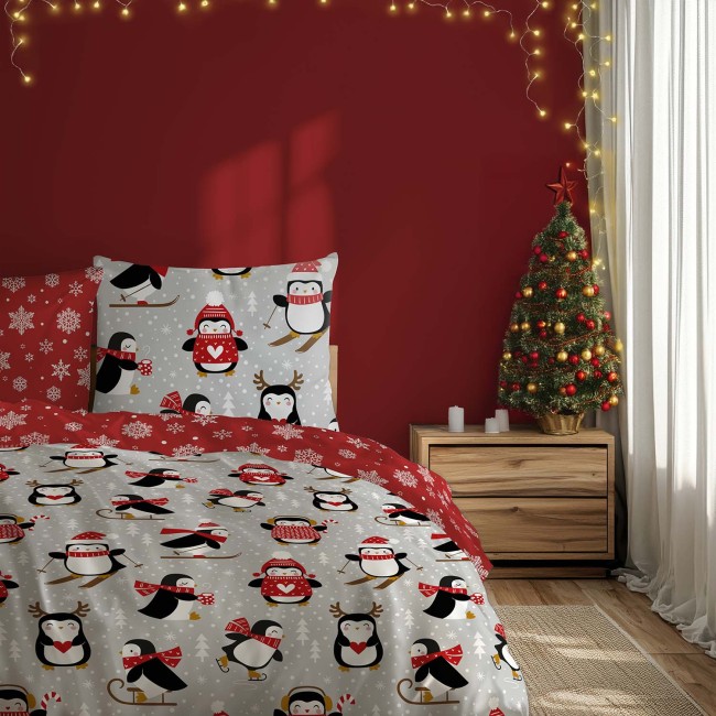 Pościel bawełniana w rozmiarze 220x200 cm z motywem pingwinów w czapkach i śnieżynkami na szarym tle. Zestaw zawiera poszewki z różnymi pingwinami, a całość harmonizuje z czerwoną ścianą i dekoracjami świątecznymi w tle.