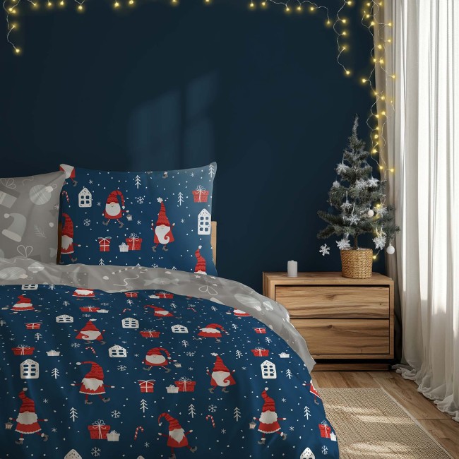 Pościel bawełniana 220x200 cm w kolorze niebieskim z wzorem czerwonych skrzatów i prezentów. Poszwa i poszewki z motywem świątecznym, leżące na łóżku, w otoczeniu dekoracyjnej choinki i drewnianego stolika.