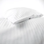 Pościel hotelowa bawełniana 140x200 z białymi pasami o szerokości 1 cm, złożona na łóżku. Widoczne poduszki w kształcie prostokątów z pasami, materiał gładki, bez ozdobnych elementów. Tło białe.
