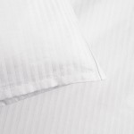 Biała poszewka na poduszkę 50x70 cm z fakturą w pionowe paski o szerokości 4 mm, leżąca na jednolitym tle. Zakończenie na zakładkę, materiał gładki, bez widocznych napisów czy logo. Wzór stonowany, pasujący do różnych aranżacji.