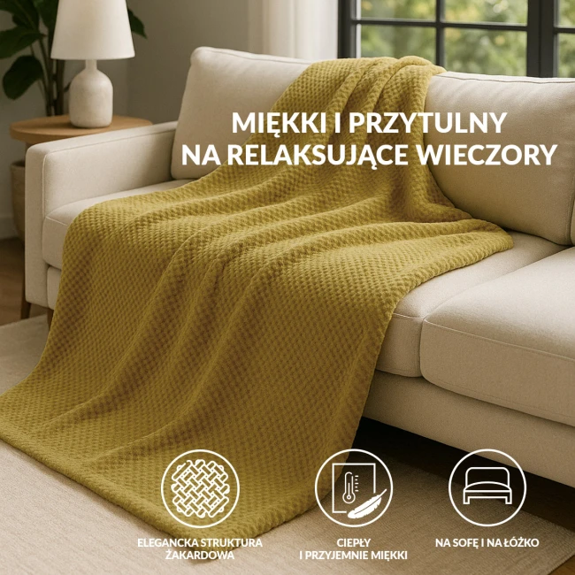 Koc żakardowy 150x200 w kolorze oliwkowym, z fakturą w formie drobnych, regularnych wzorów, leży na szarej, kanapie. W tle widoczna lampa na stoliku, co tworzy przytulny klimat aranżacji wnętrza.