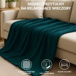 Koc żakardowy 150x200 w kolorze petrol, z fakturą w formie drobnych, regularnych wzorów, leży na szarej, kanapie. W tle widoczna lampa na stoliku, co tworzy przytulny klimat aranżacji wnętrza.