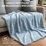 Puszysty koc dekoracyjny w jasnym niebieskim kolorze z wieloma białymi i szarymi kropkami, o wymiarach 150x200 cm, leżący na sofie. Wykonany z miękkiego materiału, idealny na relaksujące wieczory.