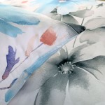 Pościel satyna bawełniana 140x200 w białym kolorze z dużymi pastelowymi niebieskimi kwiatami, widoczna poduszka z motywem kwiatowym, kąt ujęcia zbliżony, materiał gładki, elegancki wzór.