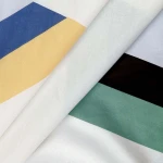 Pościel bawełniana 160x200 Rytm w kolorową geometrię, z białym tłem i pasami w kolorze niebieskim, żółtym, czarnym oraz zielonym. Materiał gładki, w ułożeniu leżącym, z widocznymi wyraźnymi krawędziami wzorów.