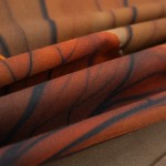 Beżowa pościel satynowa 220x240 Satynlove Premium z liściastym wzorem. Ułożona w fałdy, ukazująca gładką, połyskującą teksturę. Zbliżenie na detale wzoru z ciemnymi akcentami w kształcie gałęzi.