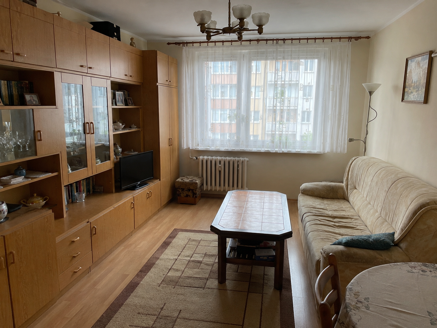Stary salon przed metamorfozą z drewnianą meblościanką, jasną kanapą i wzorzystym dywanem